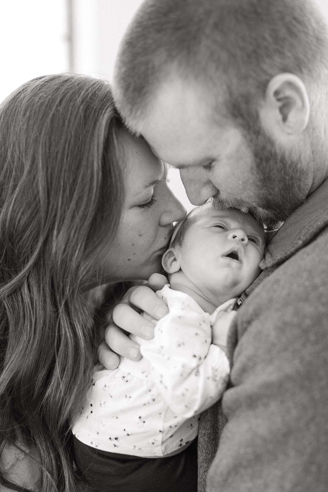 Mother & Father kissing sleeping new baby on forehead.