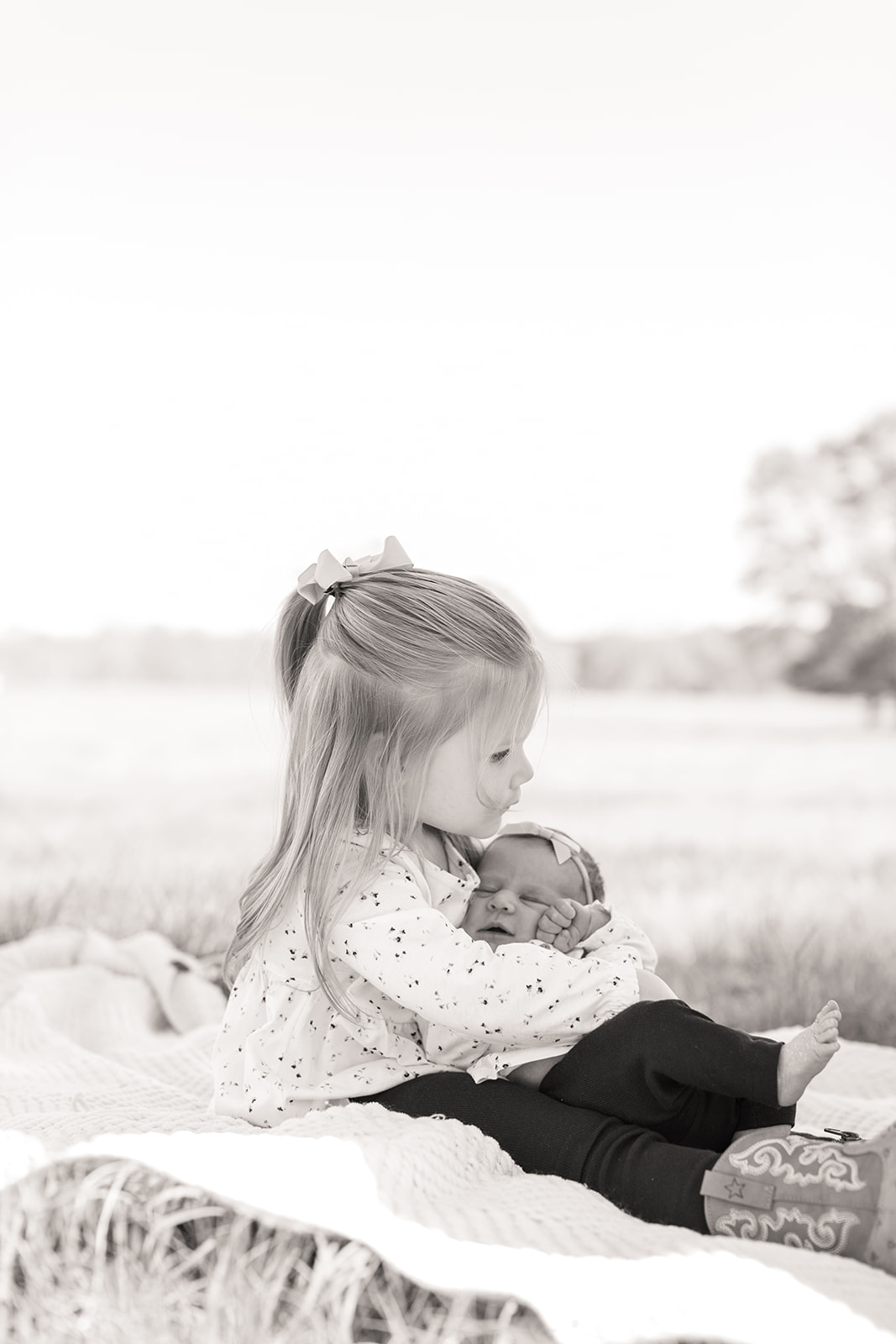 Big sister Addie gently holding her newborn baby sister in black and white photo