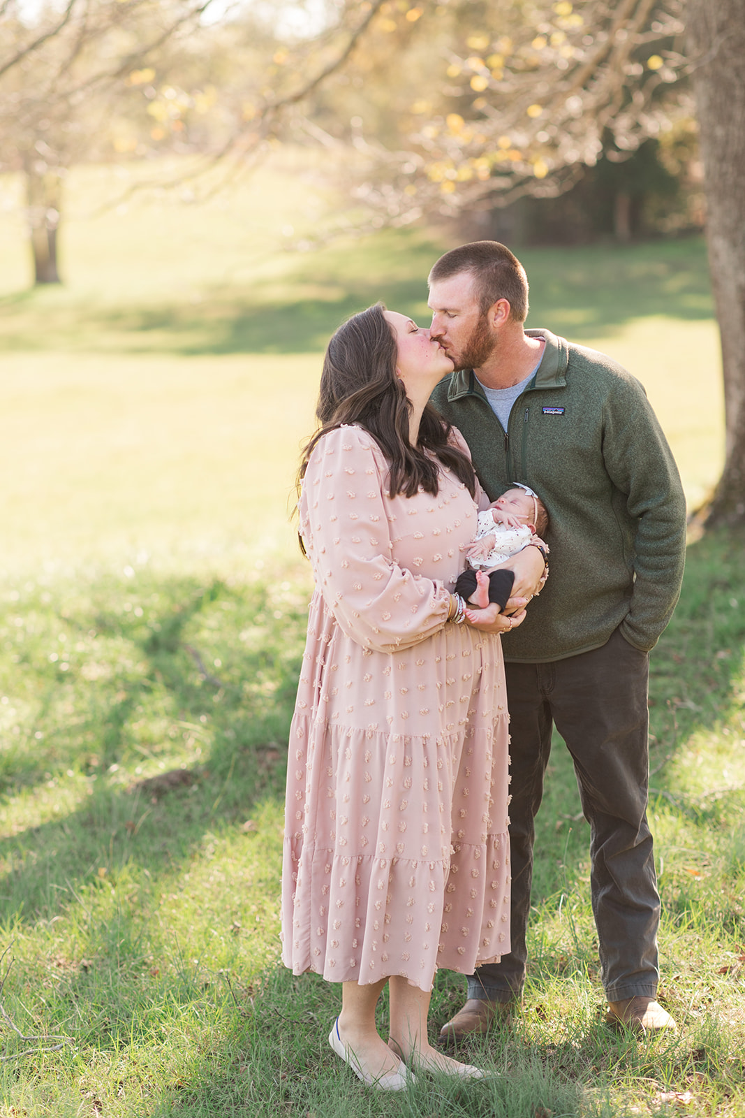 mom, dad and newborn smiling outside in natural light during newborn photography session