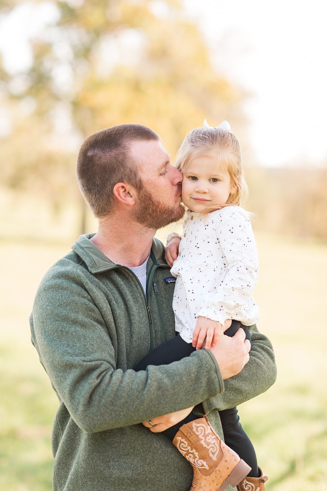 Dad kissing daughter outside in natural light during photo session