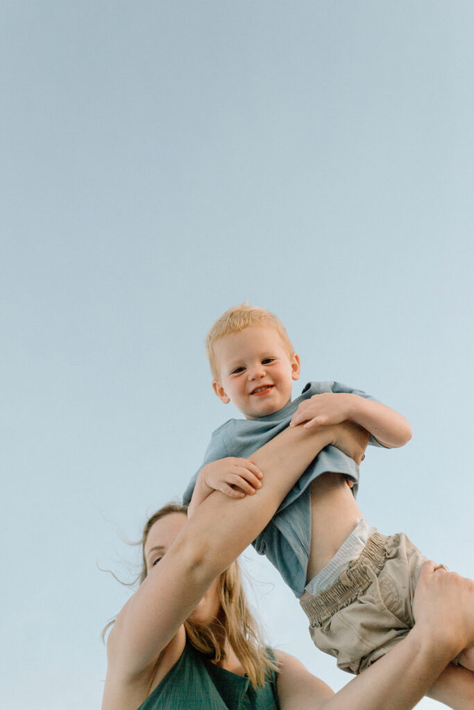 Mother lifting child into the air with ocean breeze blowing