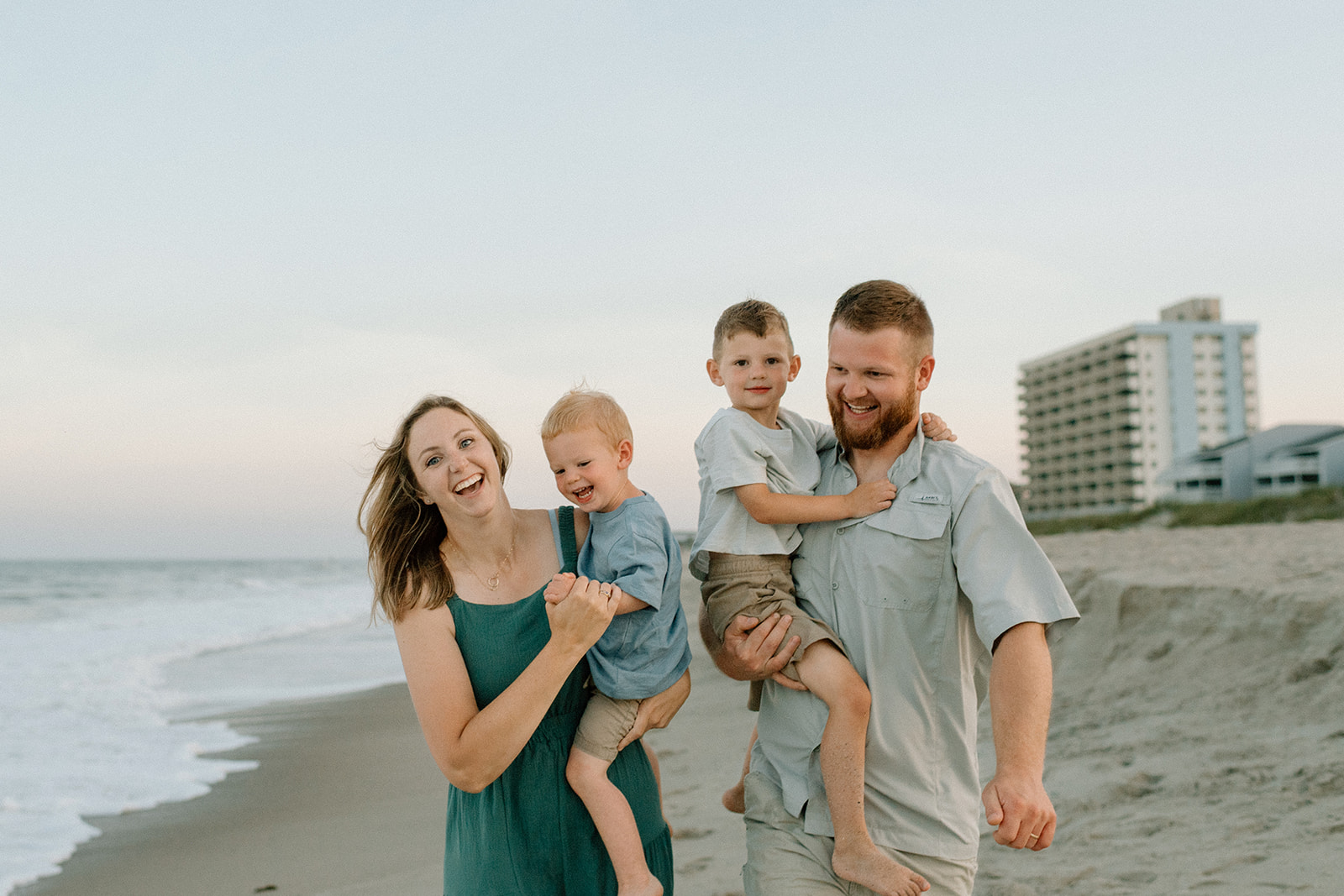 Mom and dad with two boys in their arms running on the beach at sunset.