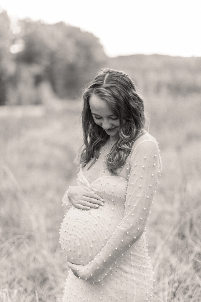 Close-up of mom-to-be’s hands cradling her baby bump with soft greenery in background.