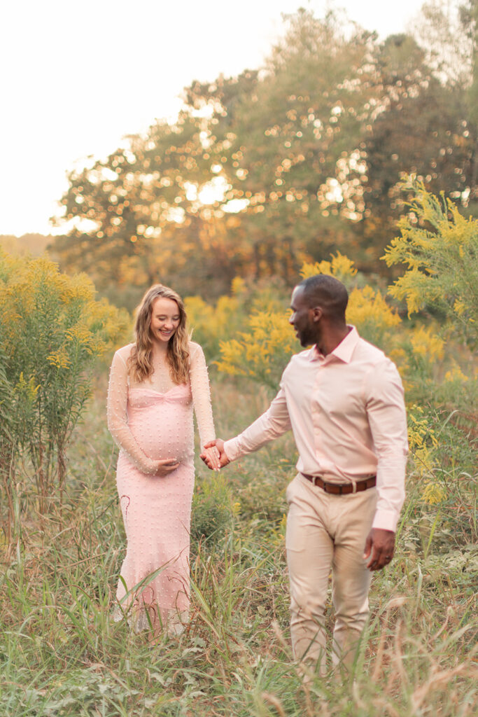 Maternity portrait with mom’s pink gown flowing in the breeze, framed by trees