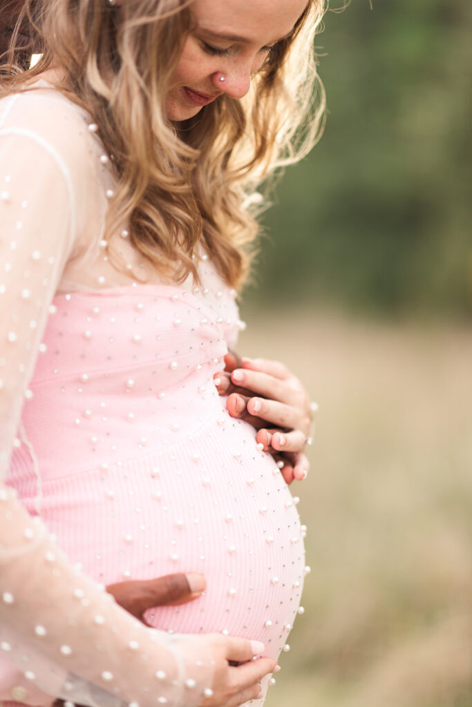 Side profile of expecting mother in pink dress with sunlight highlighting her silhouette.
