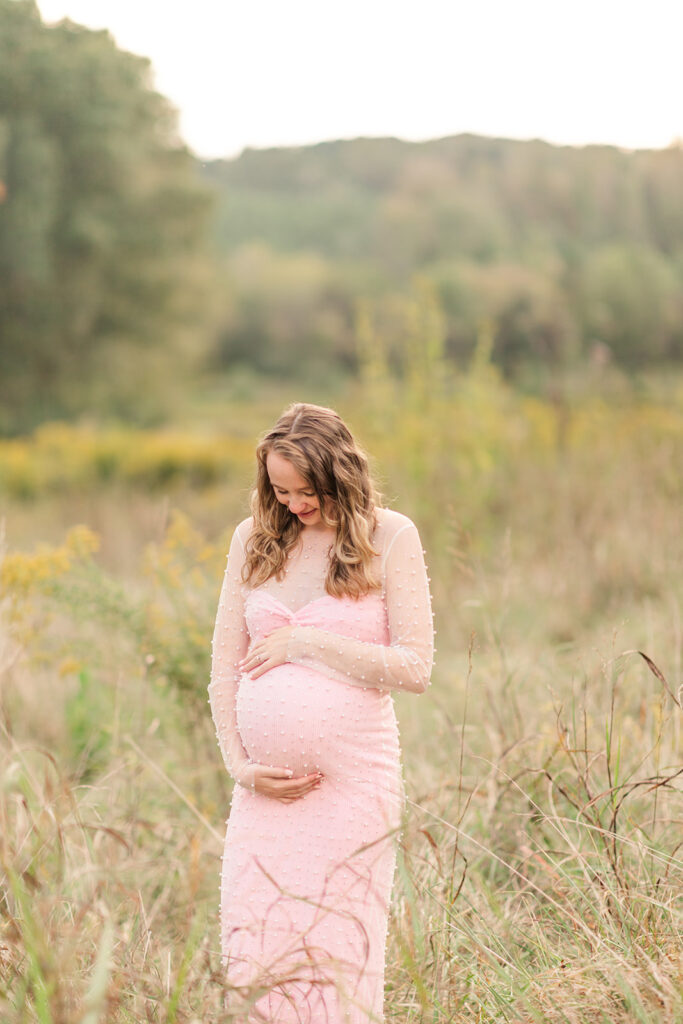 Pregnant woman standing alone, holding belly and soaking in the sunlight
