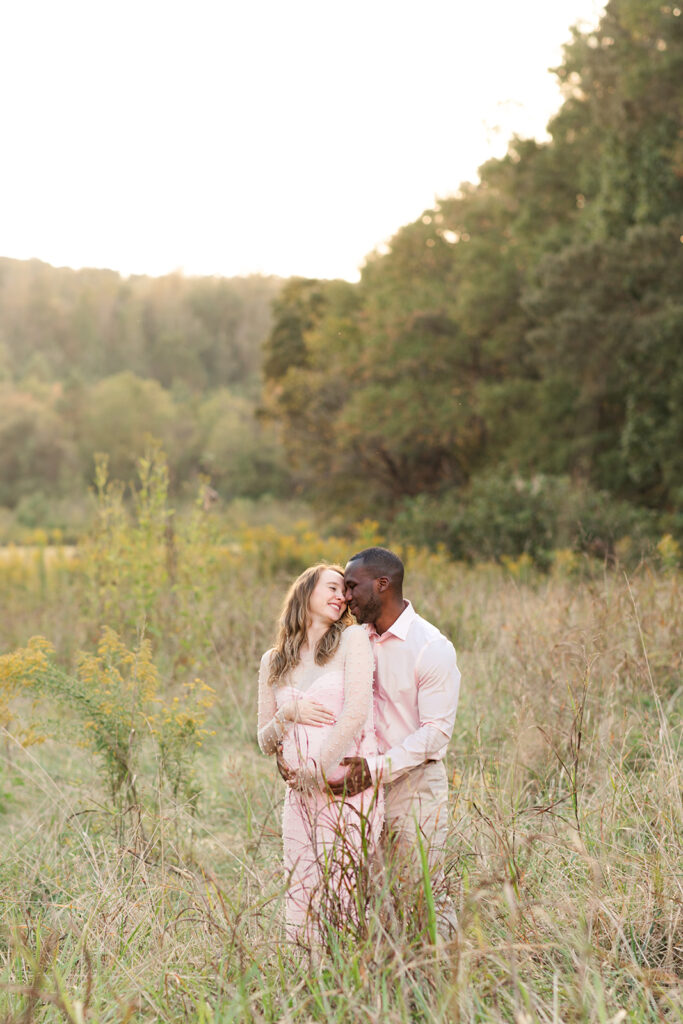 Joyful couple sharing a kiss during their maternity session in an open field.