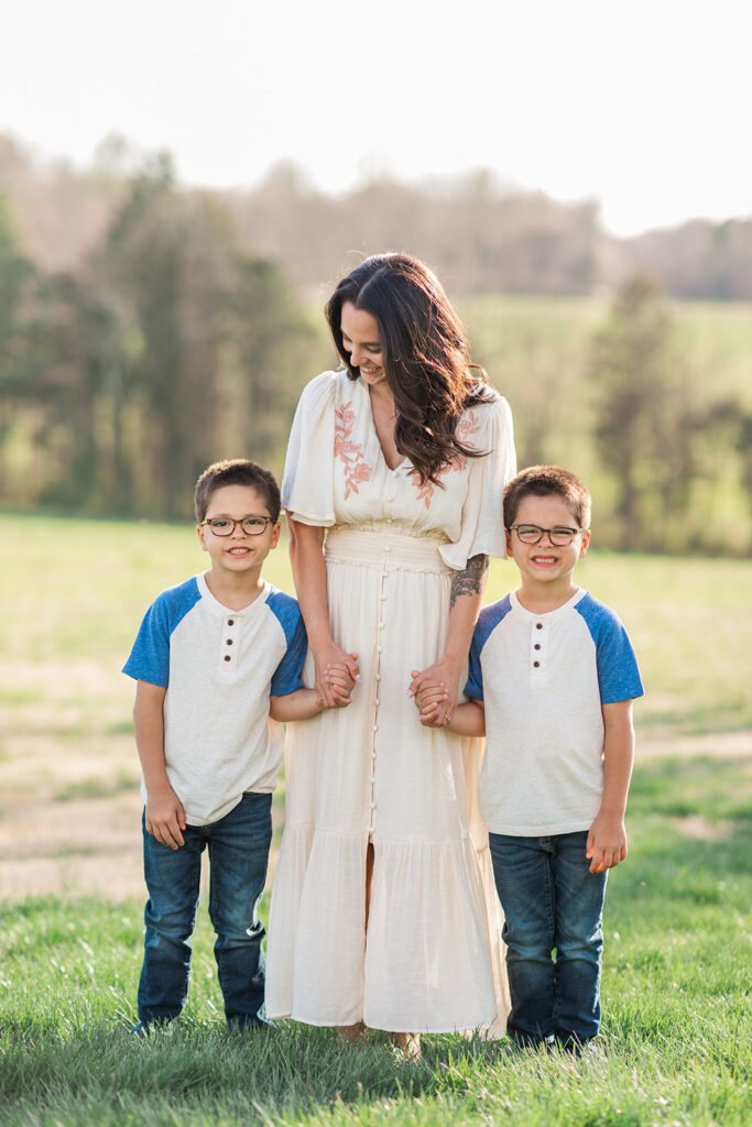 Mother and sons holding hands with natural lighting in the background of a field during family photo session mocksville NC