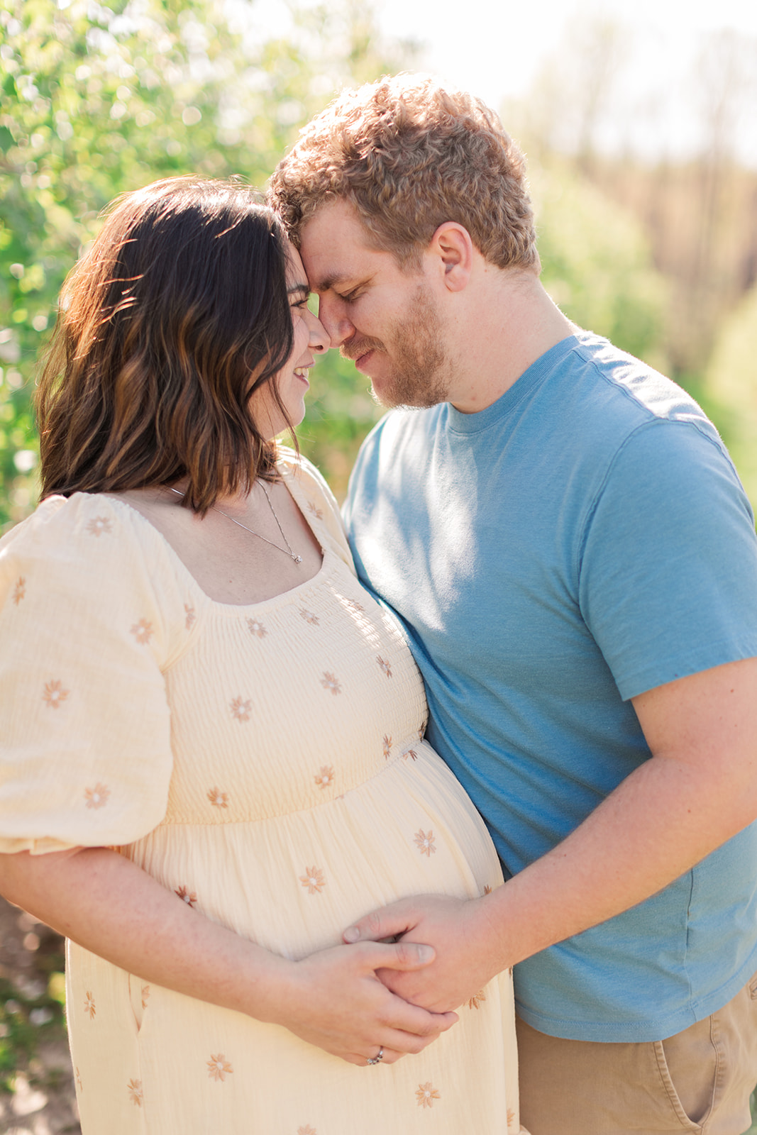 Expecting couple embracing at sunset in orchard