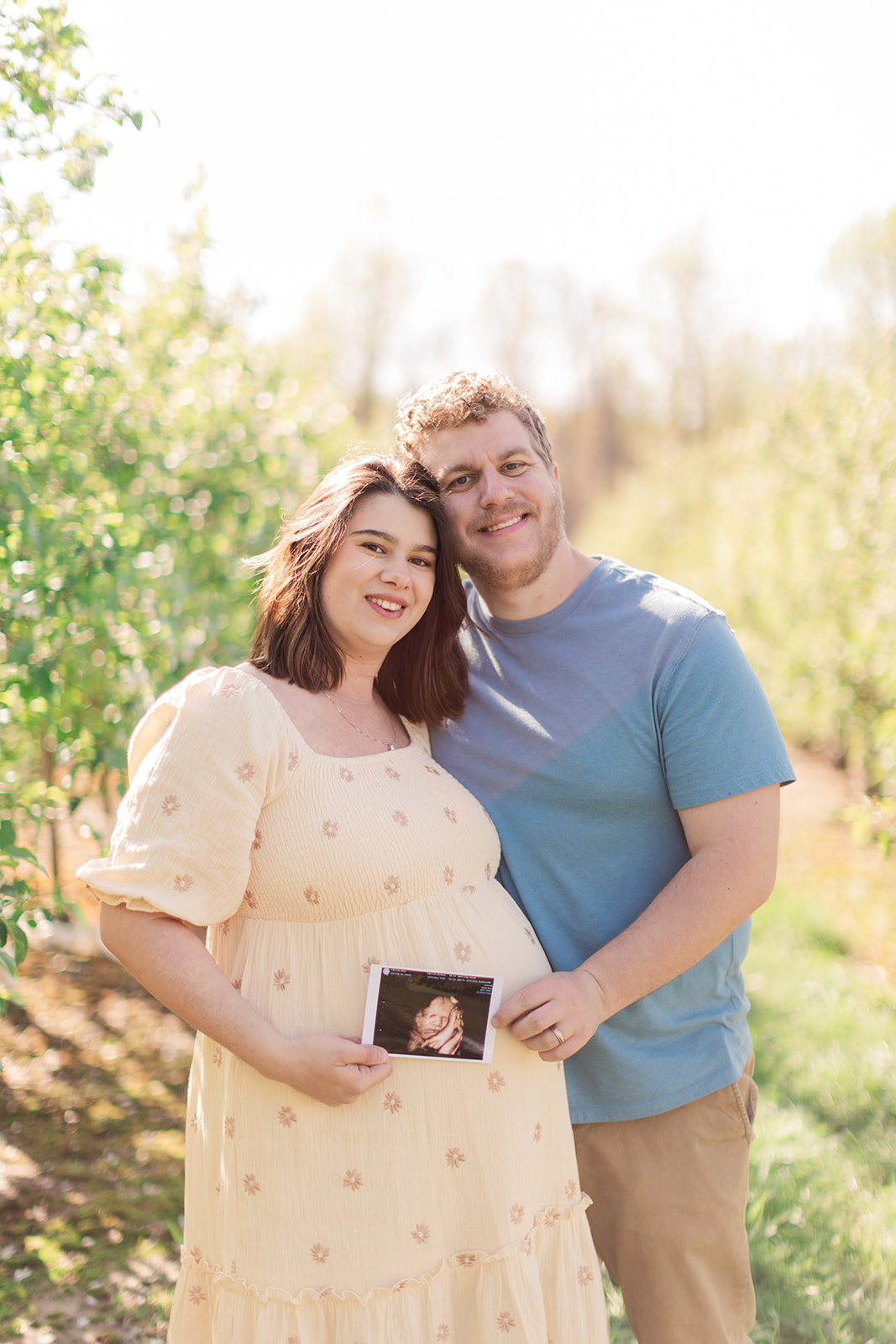 Portrait of mom-to-be and dad-to-be smiling in orchard