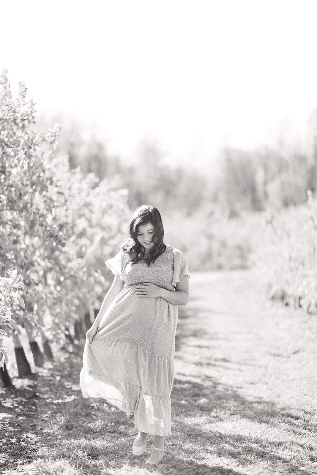 Kristi in flowing dress cradling baby bump under mountain view