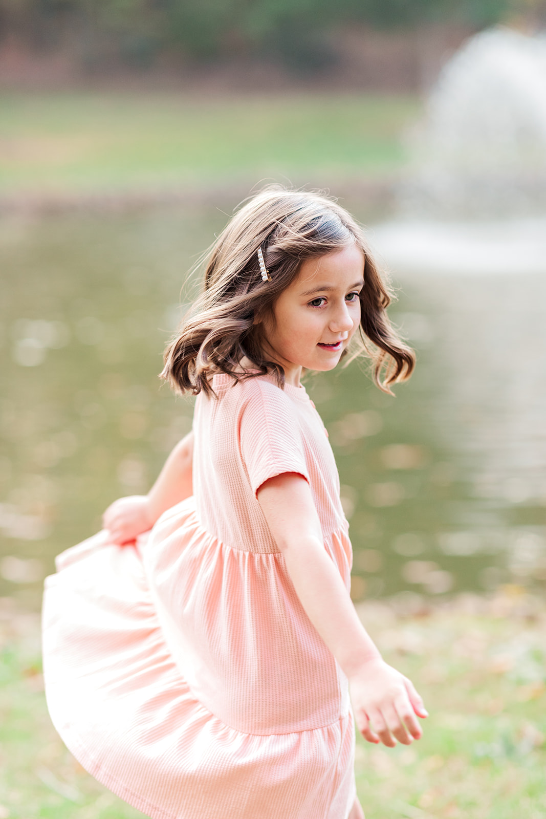 Little girl twirling in pink dress by the pond in fall at Martin Luther King Jr. Park in Statesville, NC.