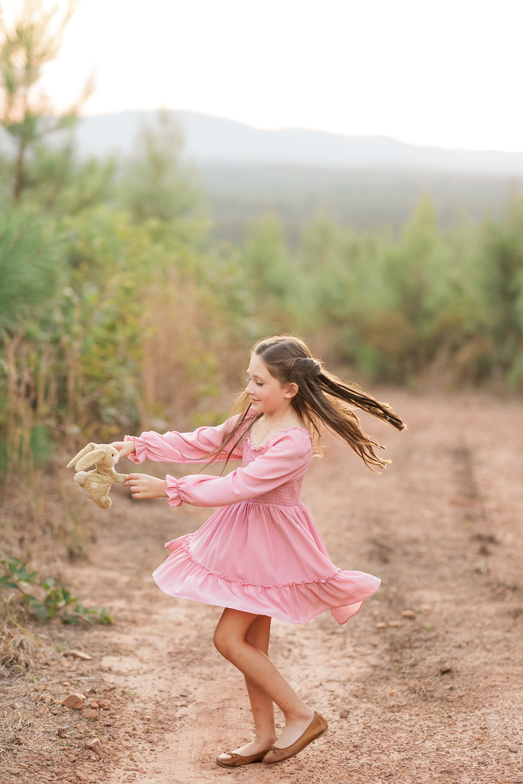 Little girl spinning in field of pines at sunset with her stuffed bunny in Taylorsville, North Carolina.