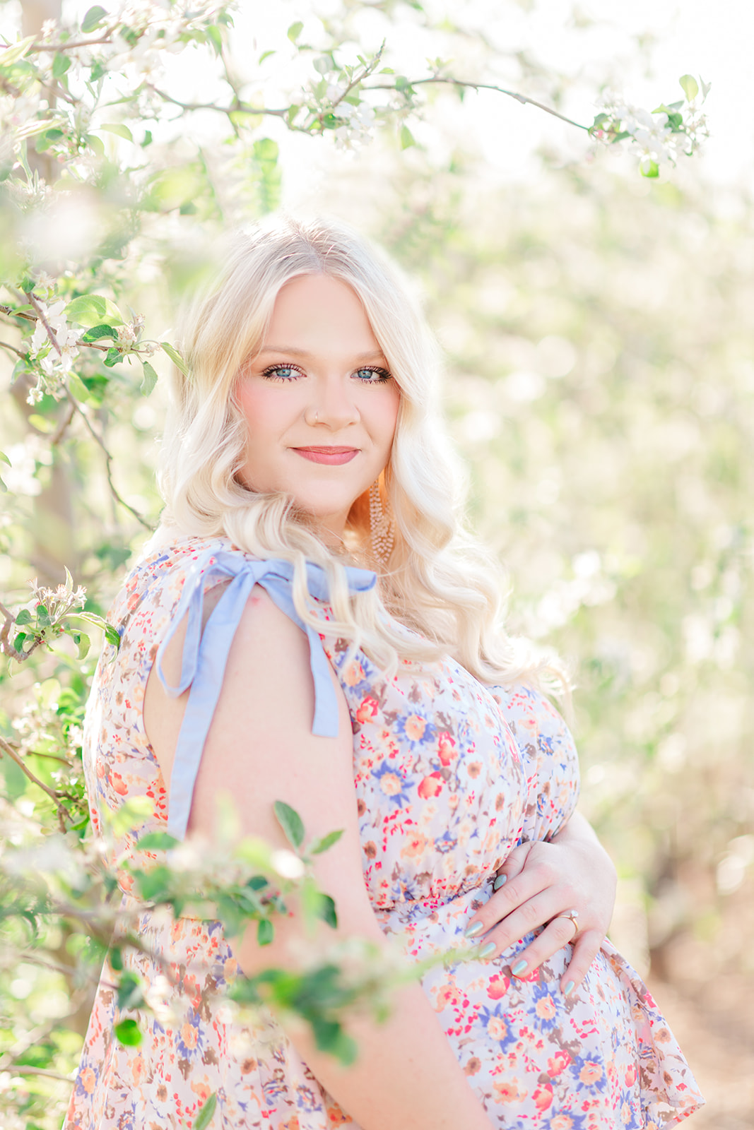 Mother-to-be in long gown posing among blooming orchard trees