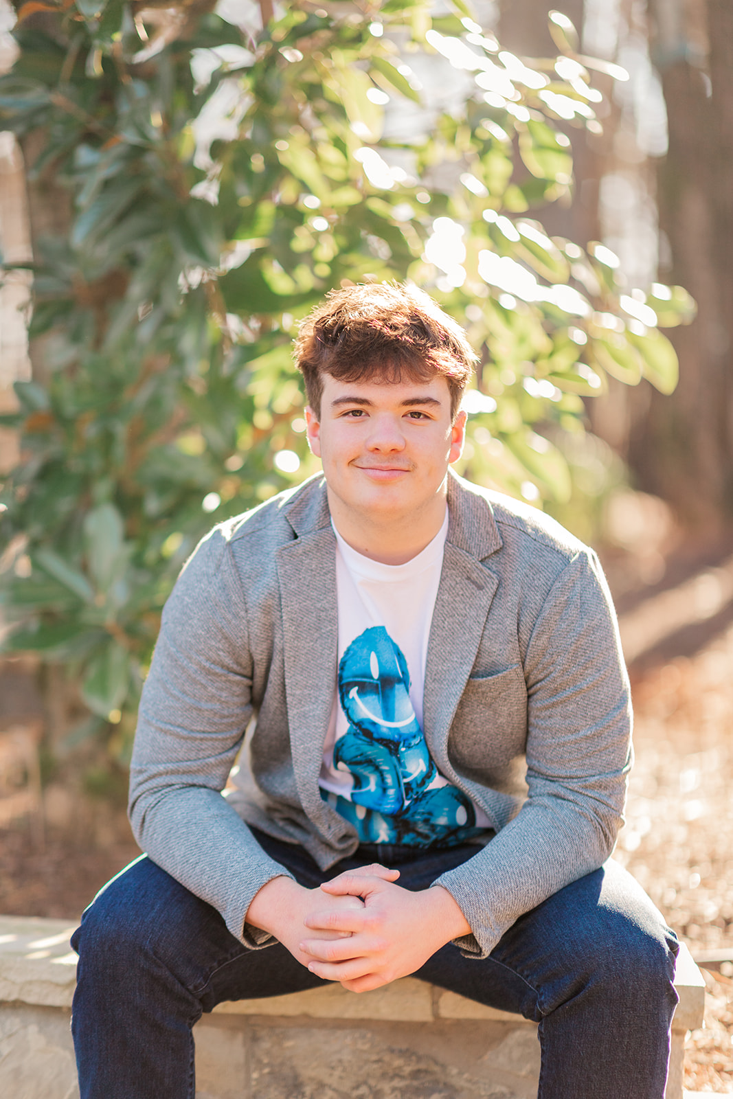 Senior boy with a white shirt featuring blue balloons sitting on a stone wall in mooresville, nc.