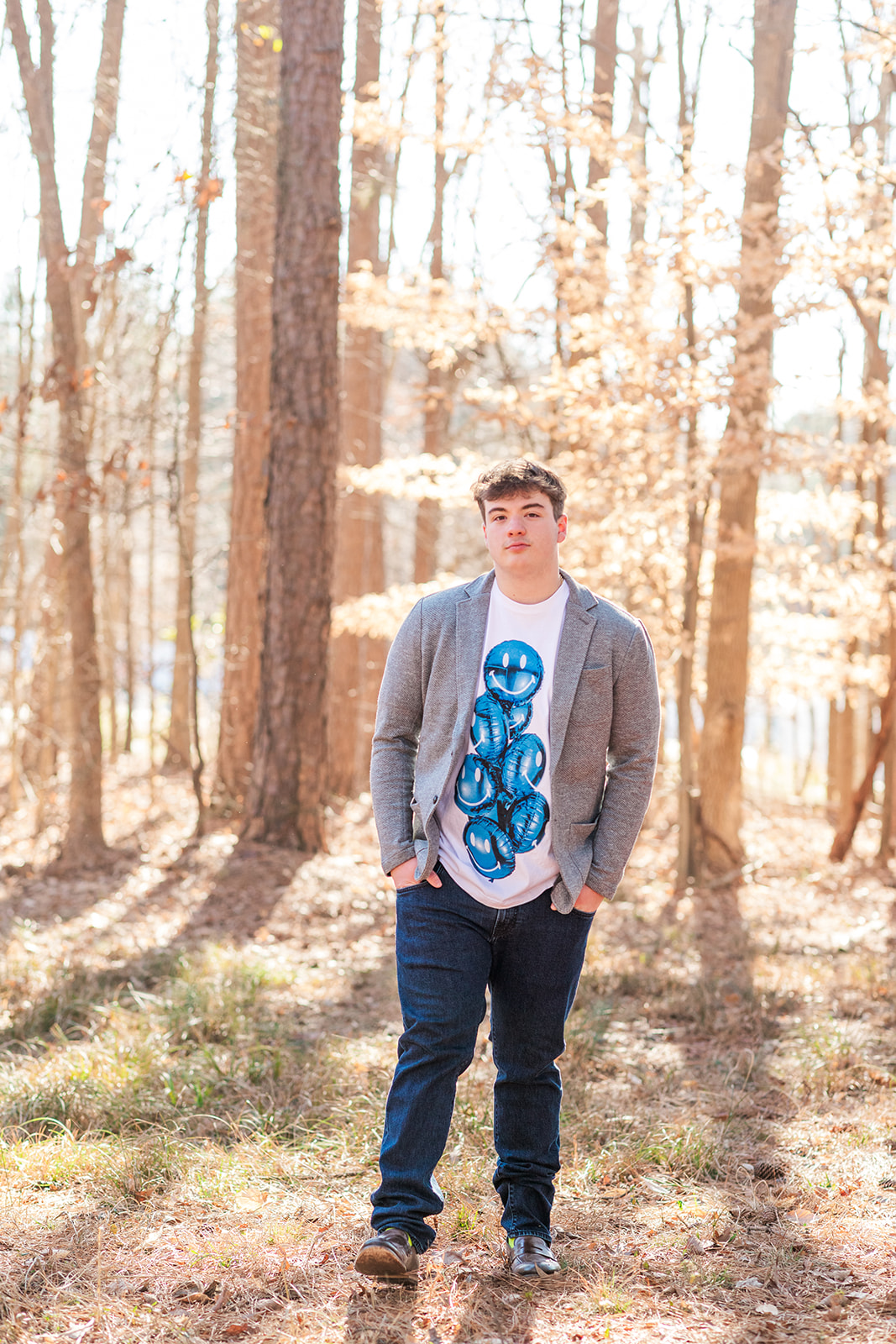 Casual senior portrait with hands in pockets, wooded background
