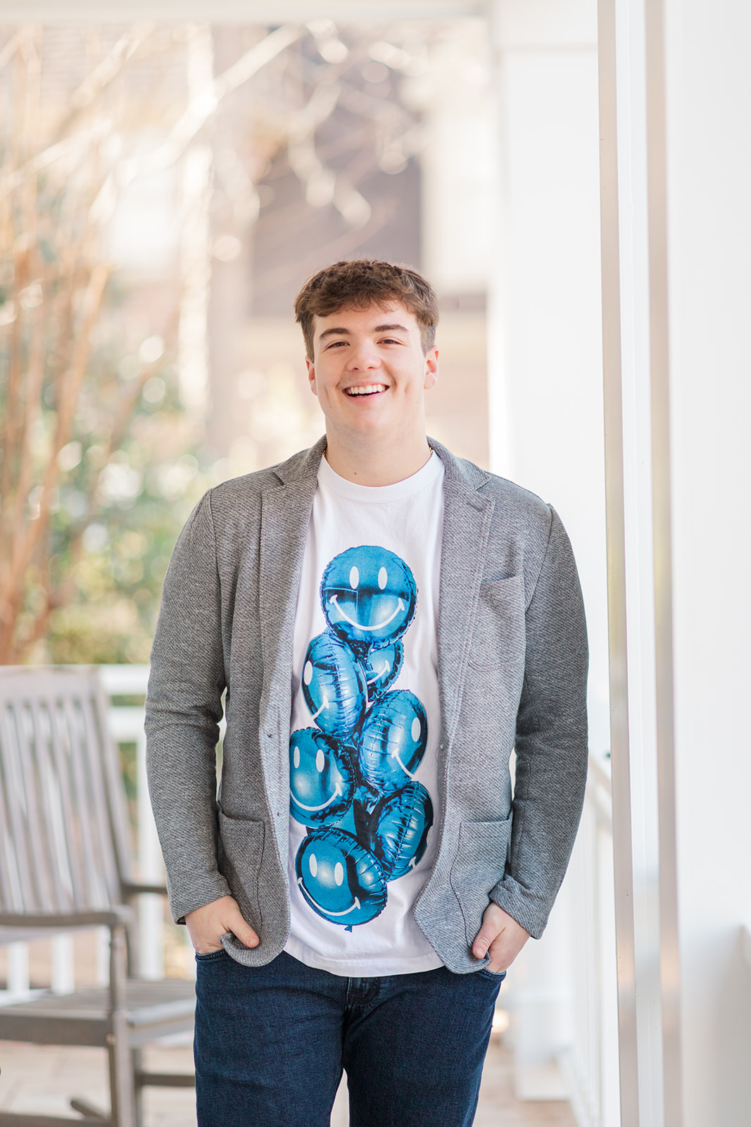 Natural light senior photo with green woods behind him on his front porch