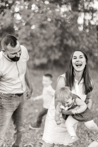 Black-and-white photo of mom swinging little girl while her two boys are running around her and her husband in North Carolina.