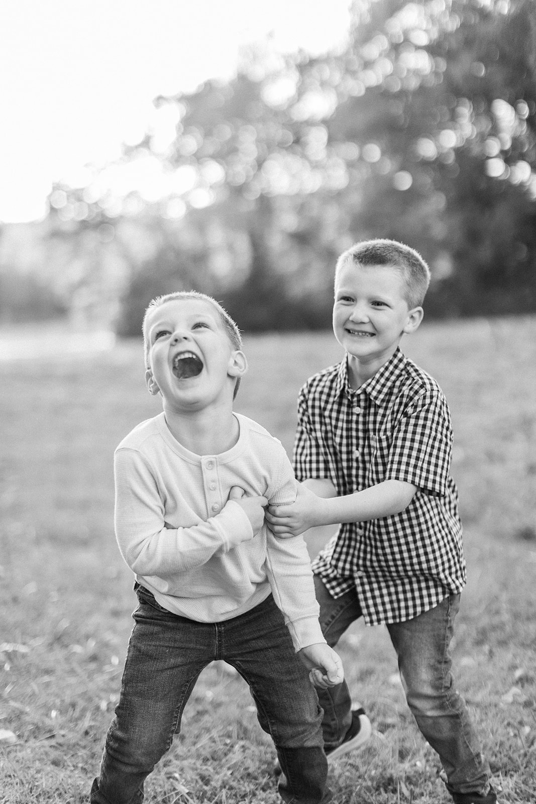Two little boys wrestling in front of the camera with smiles on their faces.