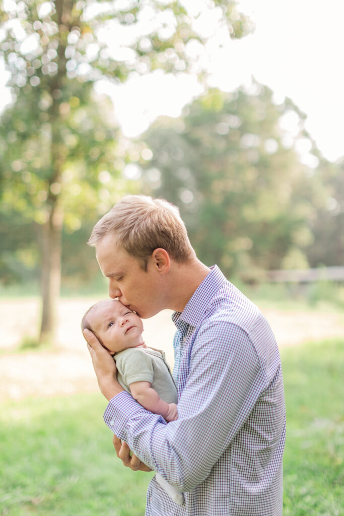 dad holding newborn baby and kissing his forehead in the morning light.