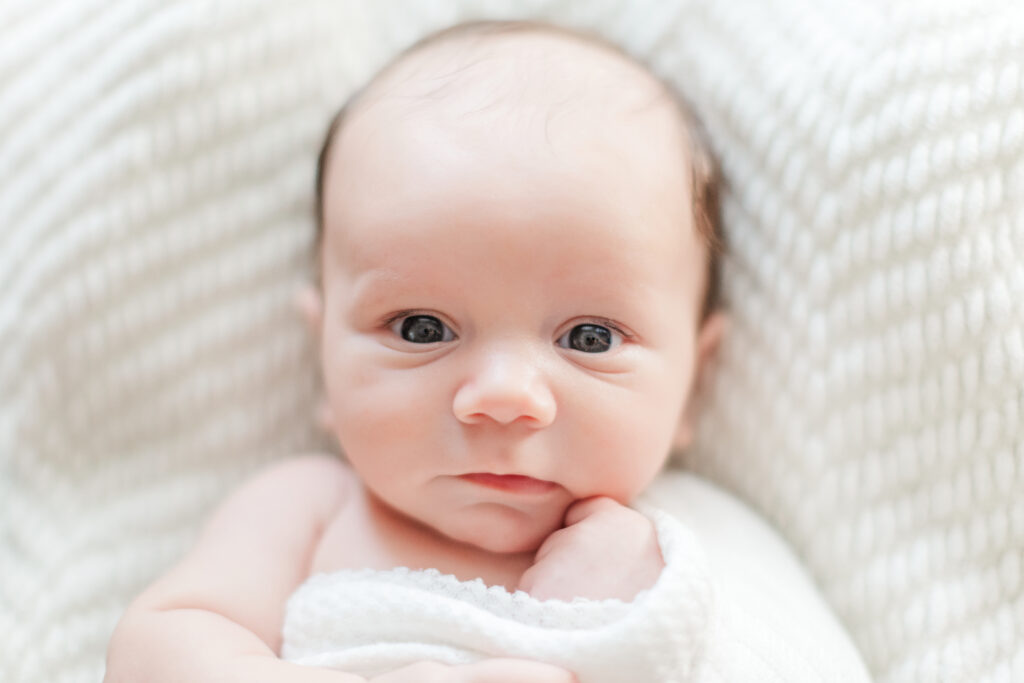 Newborn baby swaddled in white, looking right at the camera near Salisbury, NC.