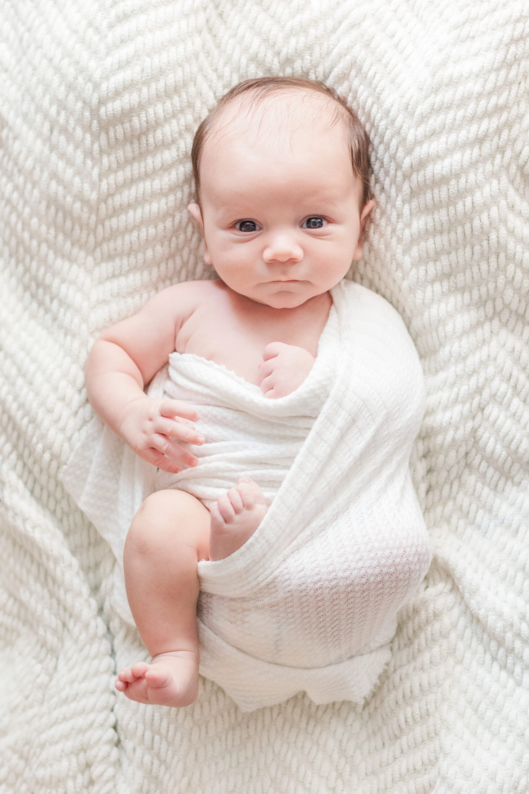 Newborn baby swaddled in white looking at the camera near Kannapolis.