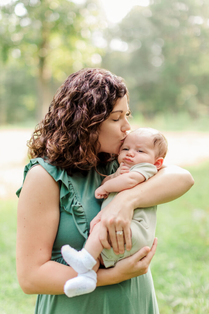 Mother kissing her newborn baby in a green dress in a field near Salisbury, NC.