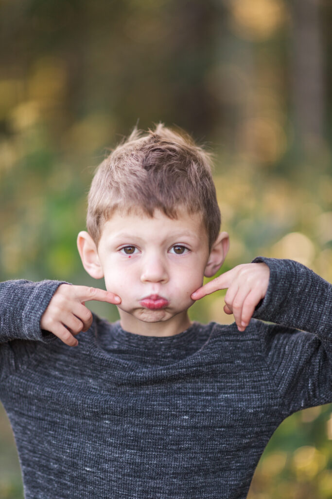 Four year old boy making silly faces in a field in fall. 