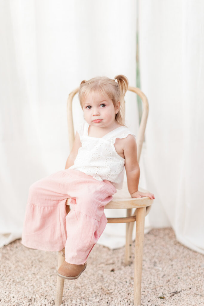 Girl sitting on a chair in greenhouse looking straight at the camera. 