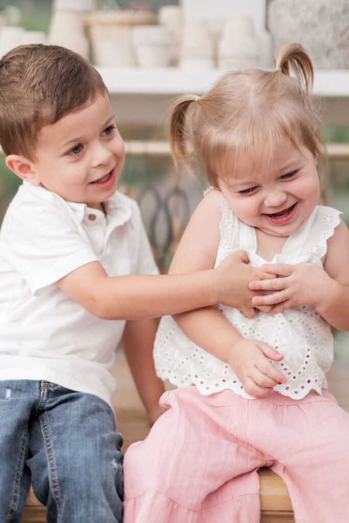 Boy tickling little girl in a candid moment after mom prepares for family photos in North Carolina. 