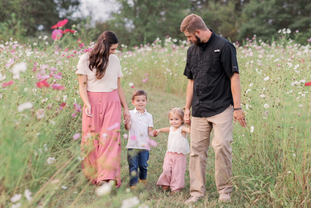 Mom and dad walking with little ones in a wildflower field during family photos at Fleurish Greenhouse in Taylorsville, North Carolina. 