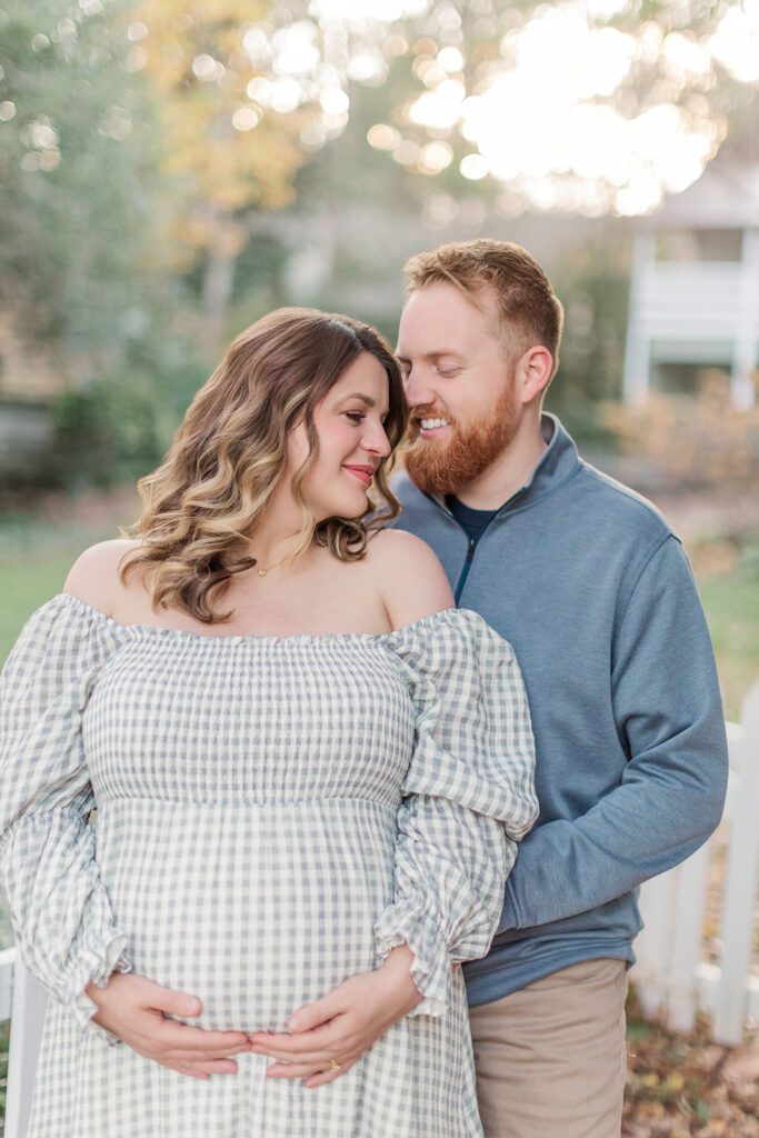 Pregnant wife looking back at husband smiling during maternity photos in the fall at Old Salem, North Carolina. 