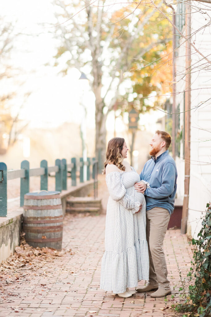 Dad has hands on mom's pregnant belly and they are laughing together at Old Salem near Winston Salem, NC.