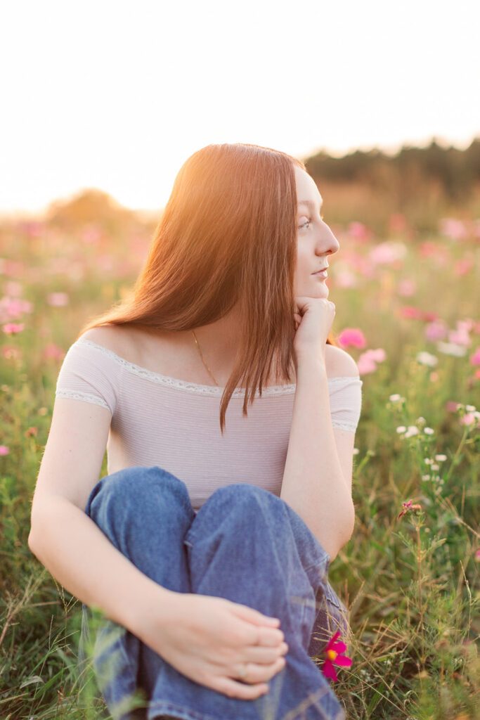 Senior girl during golden hour looking off into the distance wearing an off white timeless shirt and jeans. 