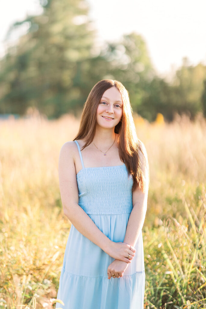 Senior girl in blue dress looking at camera in a wheat field during senior photos with Hannah Elizabeth Photography. 