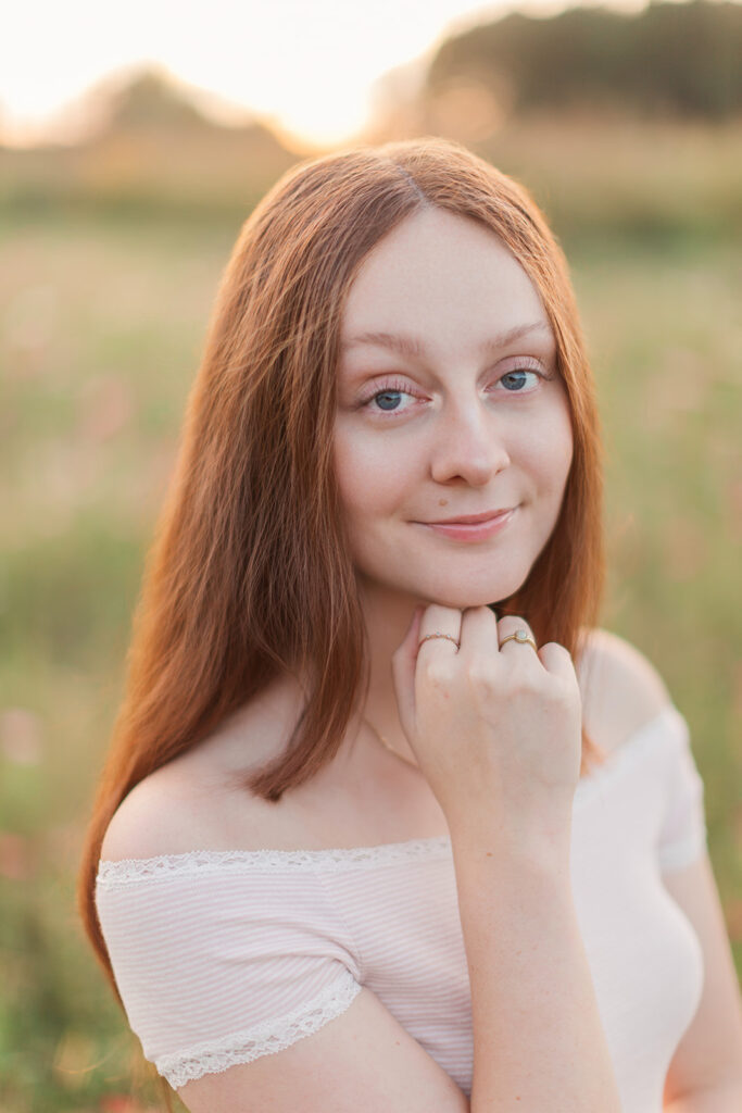 Portrait of a senior girl looking at the camera during golden hour wearing a white shirt during her senior photos with Hannah Elizabeth Photography in Statesville, North Carolina. 
