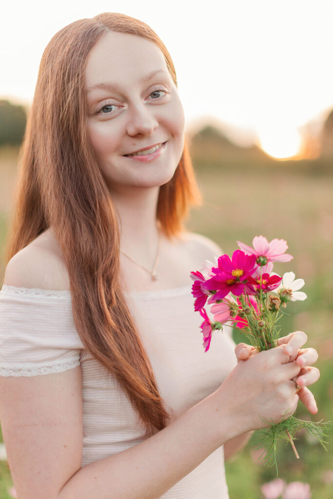Senior girl smiling and looking at the camera holding a bouquet of flowers in Windsong Flower Field in Statesville, North Carolina. 
