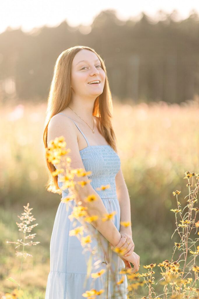 Senior girl laughing during golden hour in a blue sundress with yellow flowers during senior portraits with Hannah Elizabeth Photography in Charlotte, NC. 