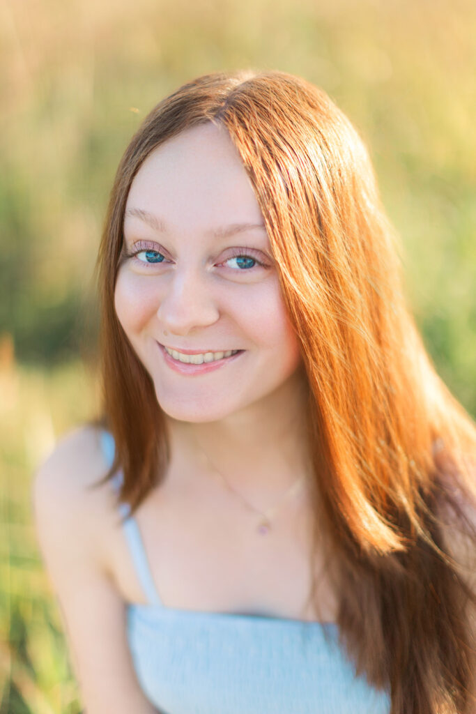 Portrait of senior girl wearing light blue dress with blue eyes during golden hour senior photos with Hannah Elizabeth Photography. 