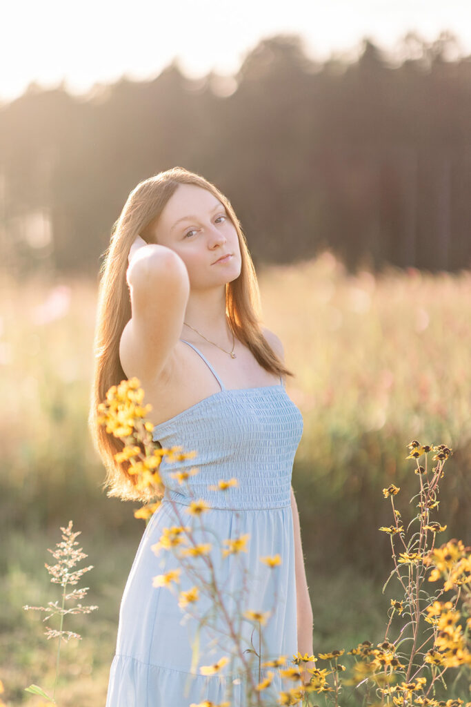 Senior girl knowing what to wear during her senior photos with a blue dress looking at camera running her hands through her hair. 